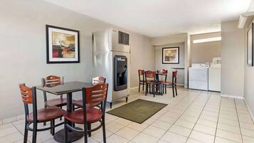 A compact kitchen with a refrigerator, microwave, and a washing machine. There are two dining areas with chairs and tables.