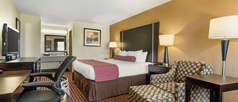 A hotel room with a bed, desk, chair, and a TV.