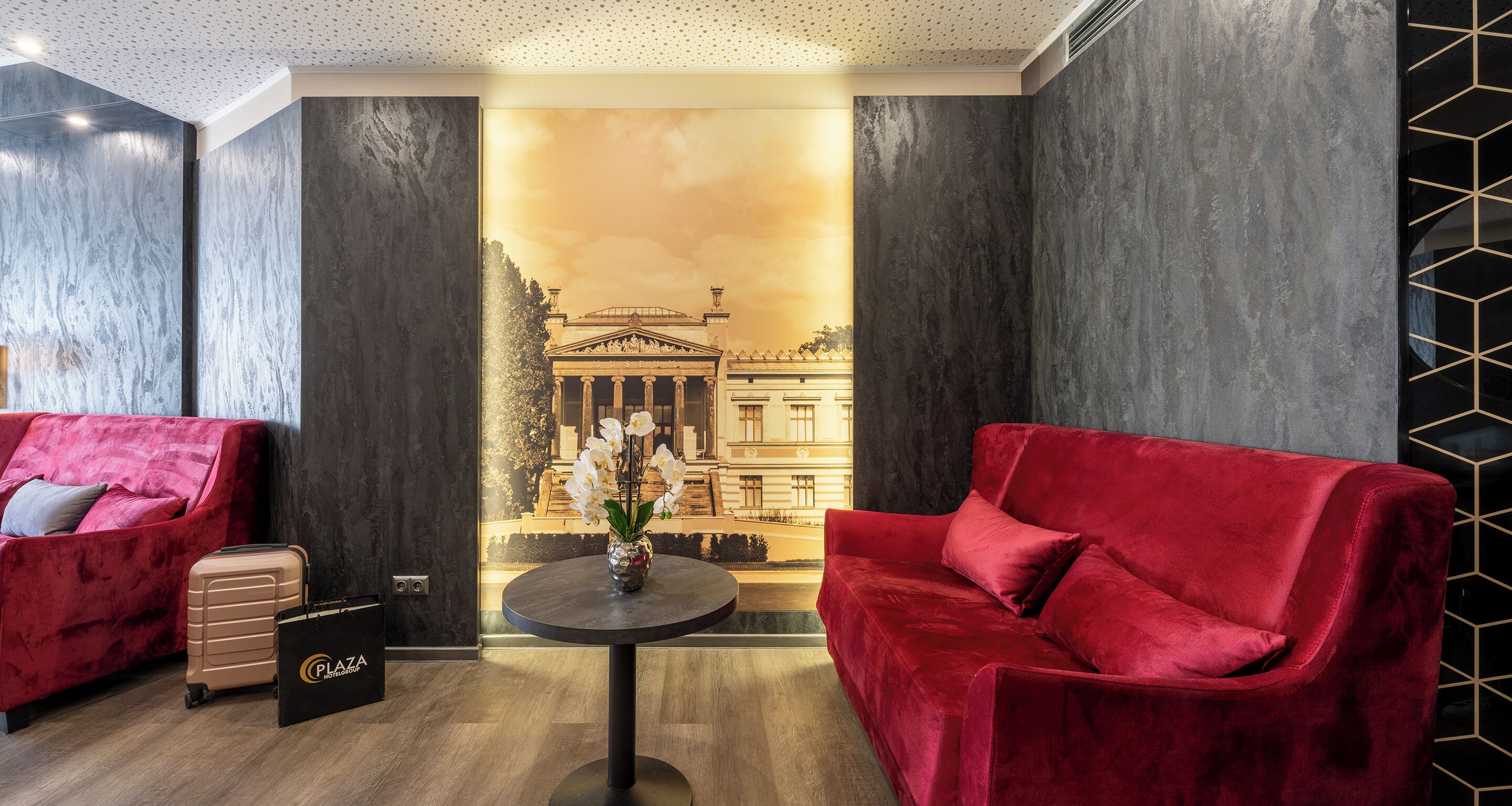 Un hall d’hôtel moderne avec un canapé rouge, un fauteuil noir et une petite table sur laquelle est posé un vase de fleurs.