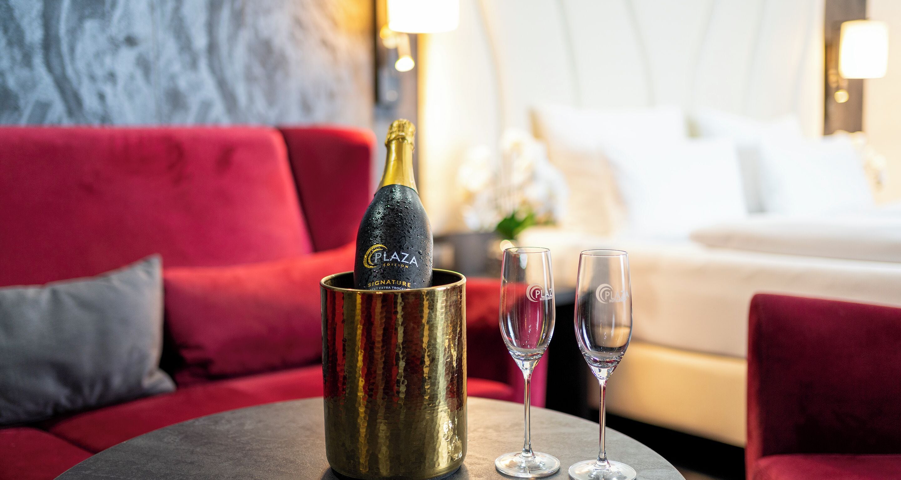 A minibar with a bottle of champagne and two glasses on a table in a hotel room.