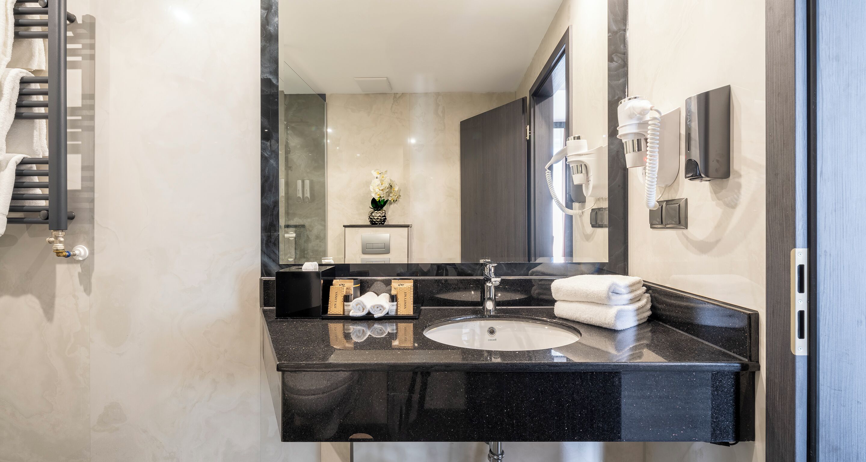A modern bathroom with a black granite countertop, a white sink, a towel rack, and a mirror.