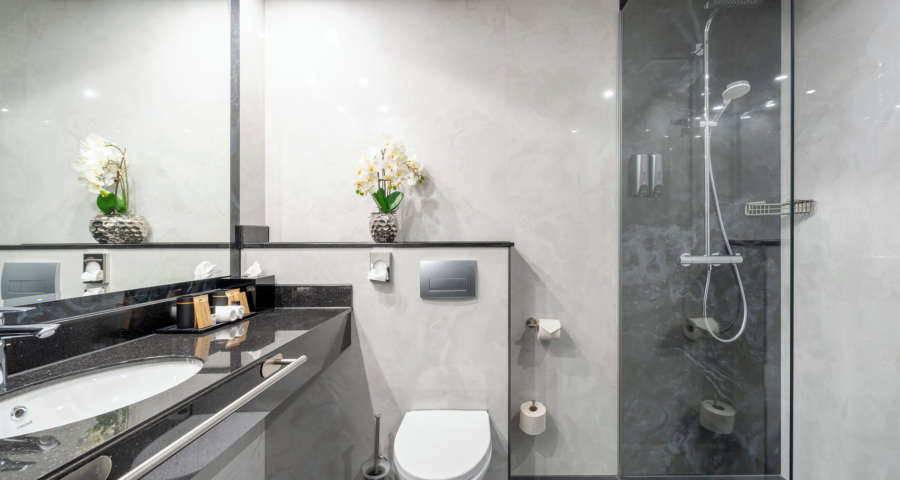 A modern bathroom with a glass-enclosed shower, a white toilet, and a black countertop with a sink.