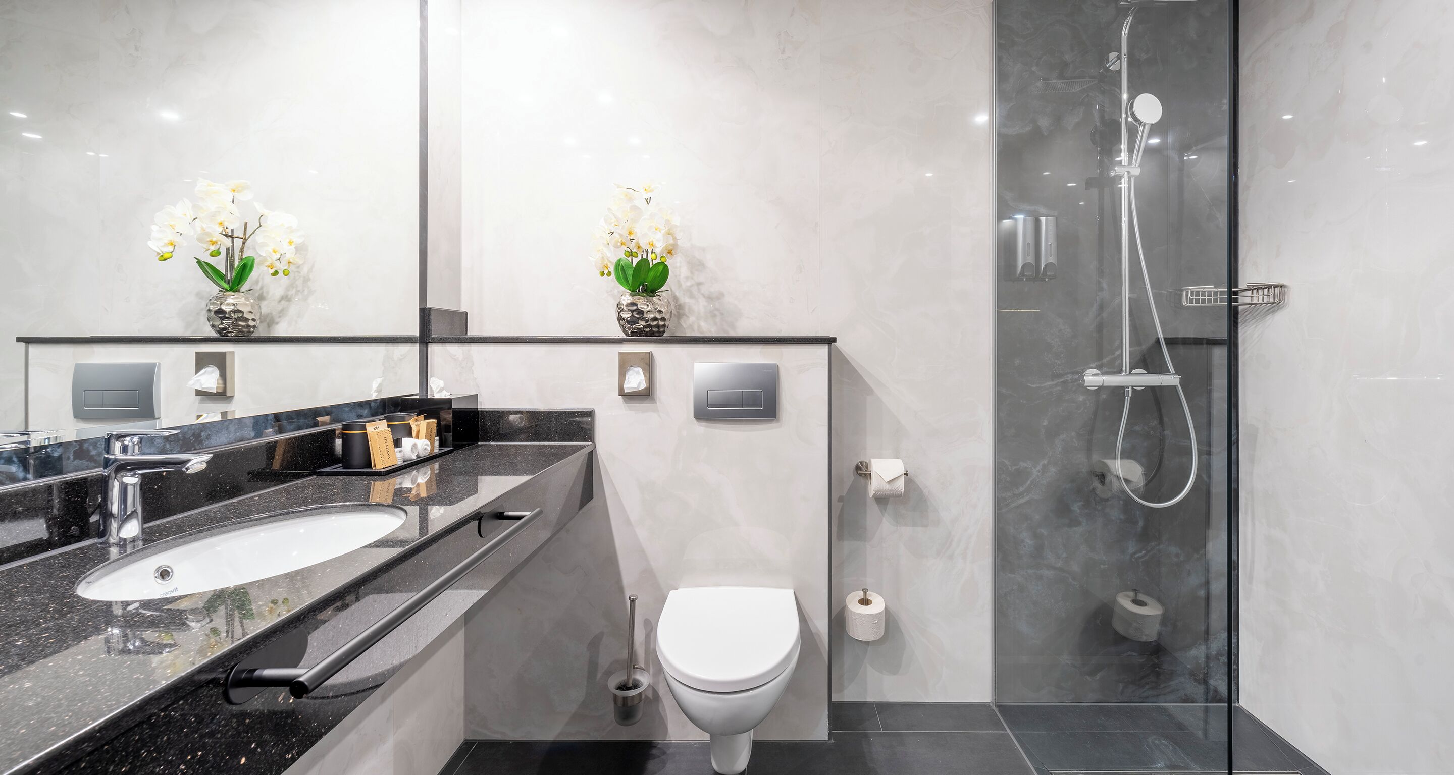 Een moderne badkamer met een zwart aanrecht, een wastafel, toilet en een douchecabine met glazen wanden.