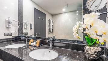 Un baño moderno con dos lavamanos, un espejo grande y un florero con flores blancas.