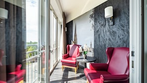 Un balcon avec des fauteuils en cuir rouge, une petite table ronde ornée d’un vase de fleurs et une vue sur la ville à travers de grandes fenêtres.
