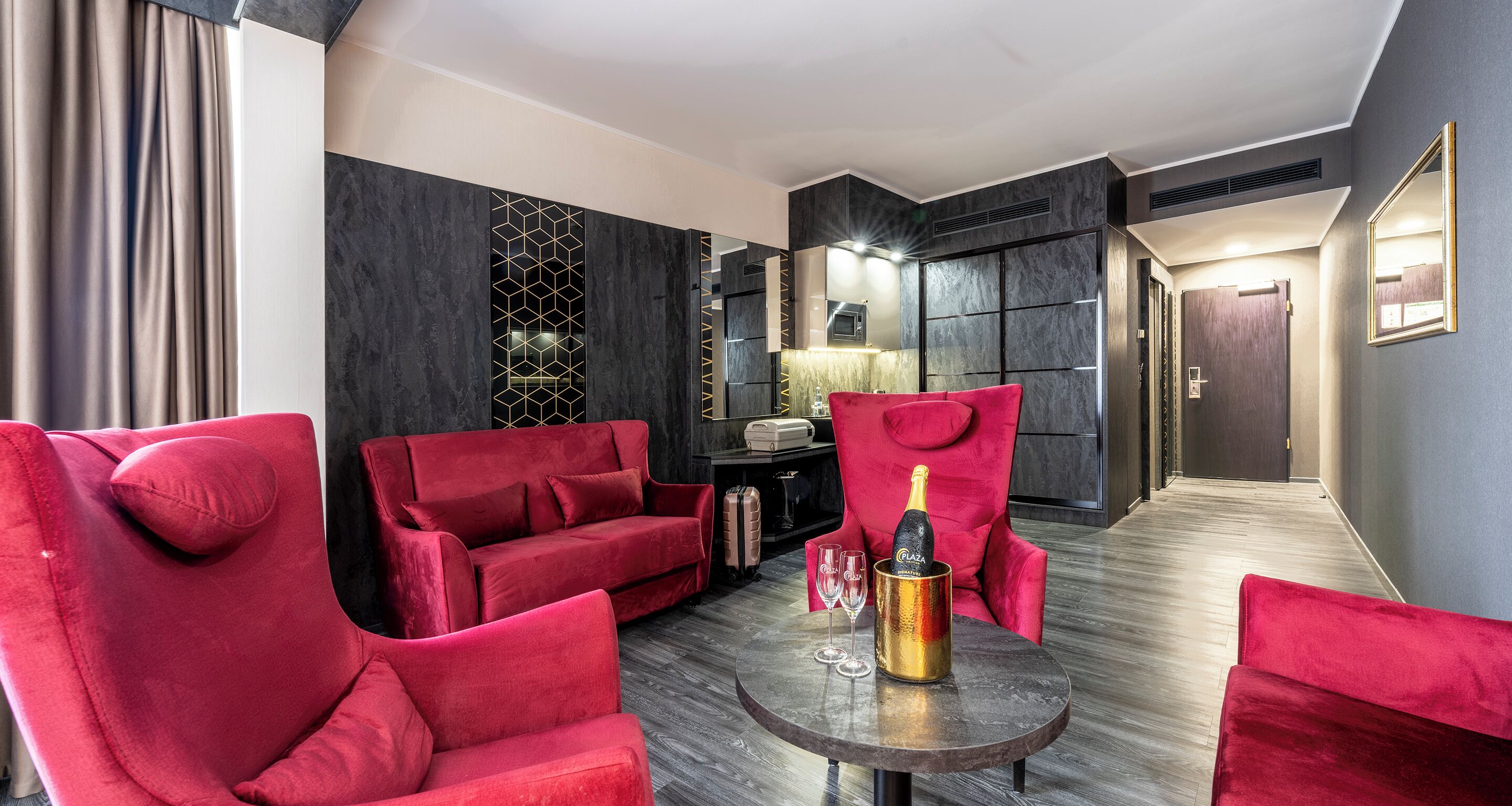 A modern living room with red velvet sofas, a round table with a champagne bottle, and a decorative wall panel.