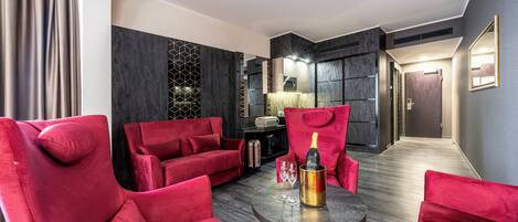 A modern living room with red velvet sofas, a round table with a champagne bottle, and a decorative wall panel.