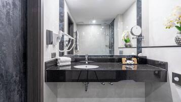 A modern bathroom with a black marble countertop, a sink, a mirror, a hairdryer, and a vase with white flowers.
