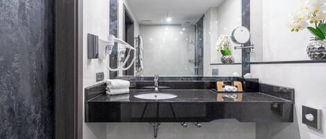 Een moderne badkamer met een zwarte marmeren aanrecht, een wastafel, een spiegel, een haardroger en een vaas met witte bloemen.