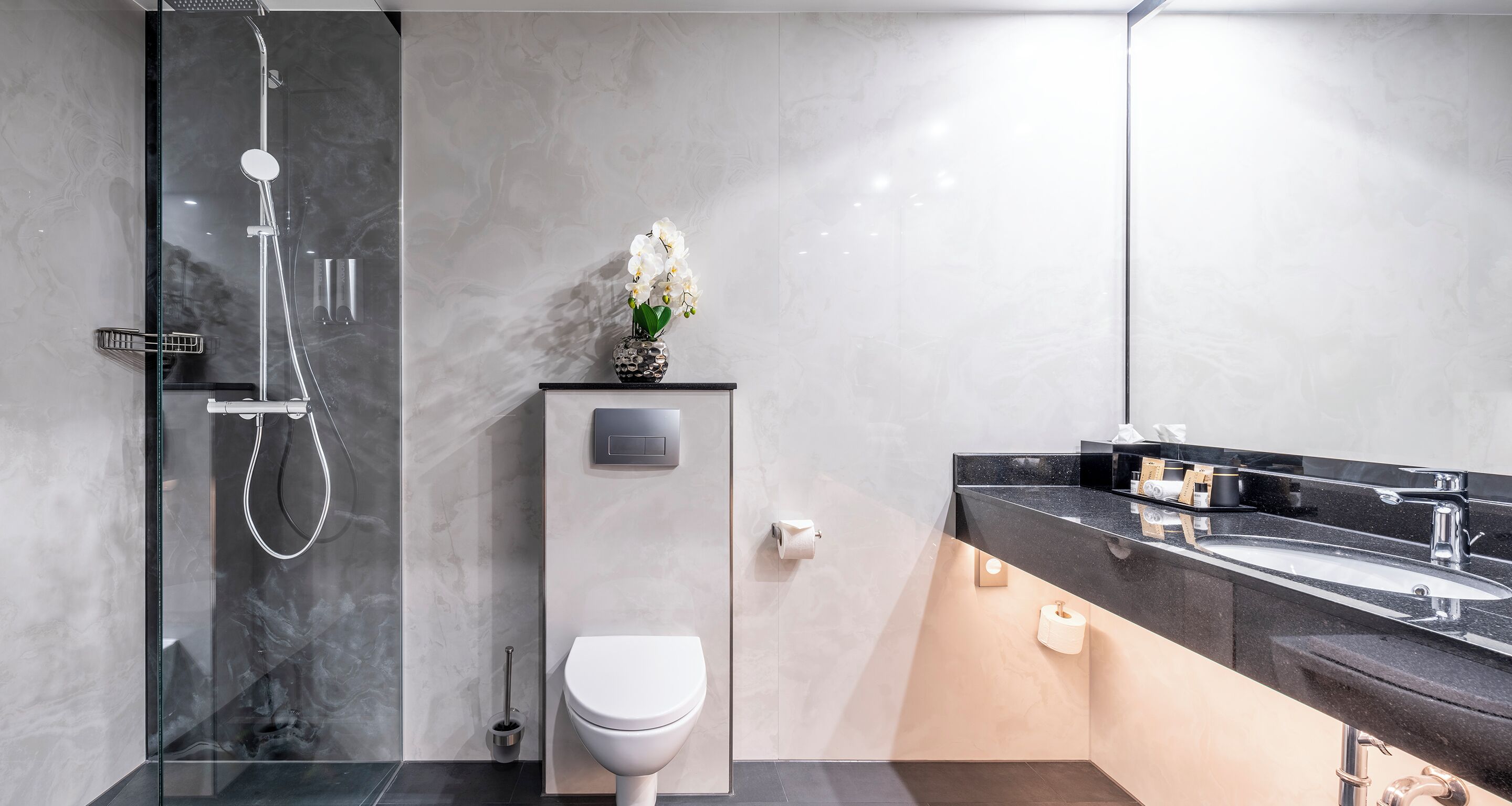 Une salle de bain moderne dotée d’une douche à parois de verre, de toilettes et d’un meuble-lavabo avec un évier et un miroir.