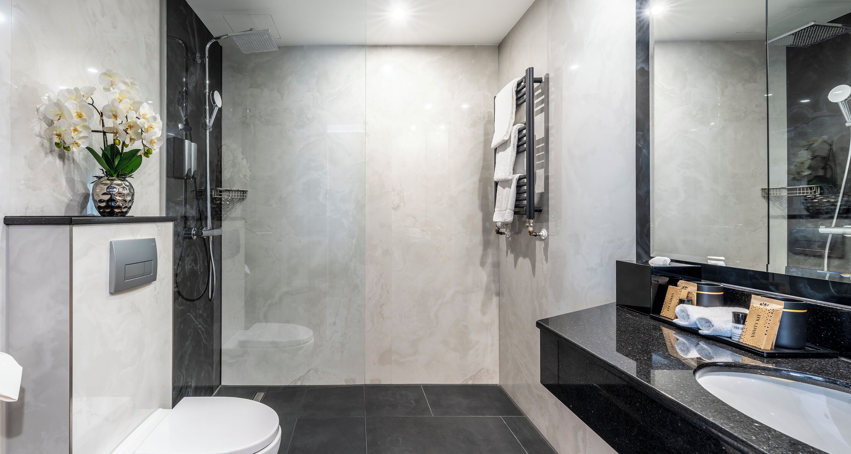 Une salle de bain moderne avec une douche à parois de verre, des toilettes blanches, un meuble-lavabo noir avec un plan de travail noir et un miroir.