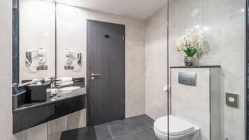 Un baño moderno con puerta de madera oscura, mampara de ducha de vidrio y un inodoro blanco.