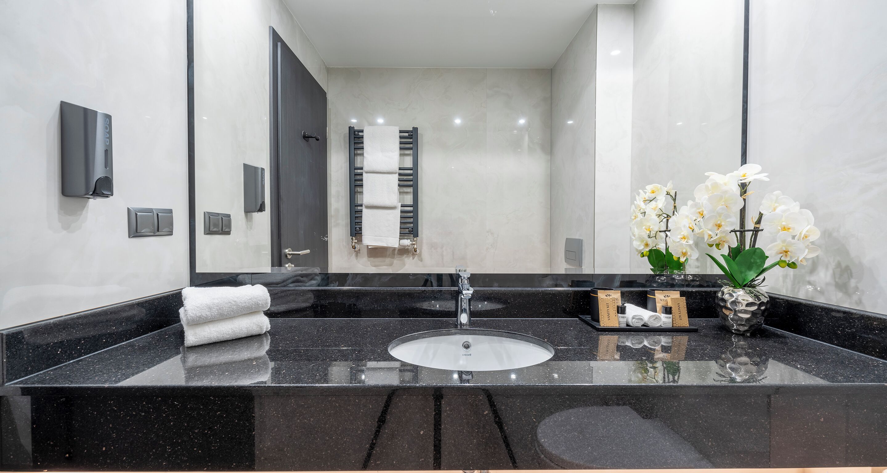 A modern bathroom with a black granite sink, a towel rack, and a vase with white flowers.