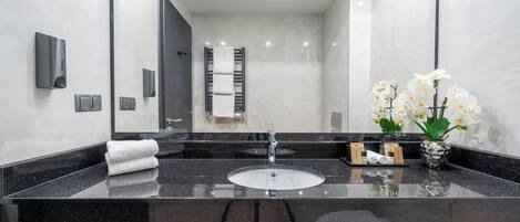 A modern bathroom with a black granite sink, a towel rack, and a vase with white flowers.