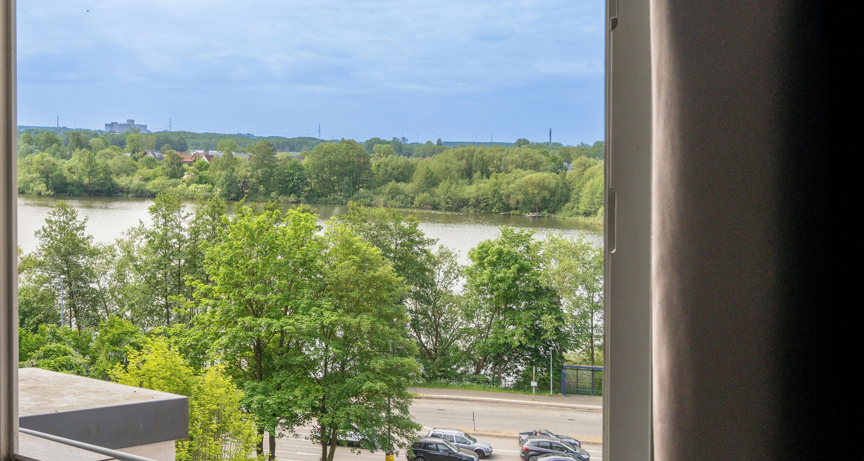 Vista desde una ventana sobre un río, árboles y un paisaje urbano distante.