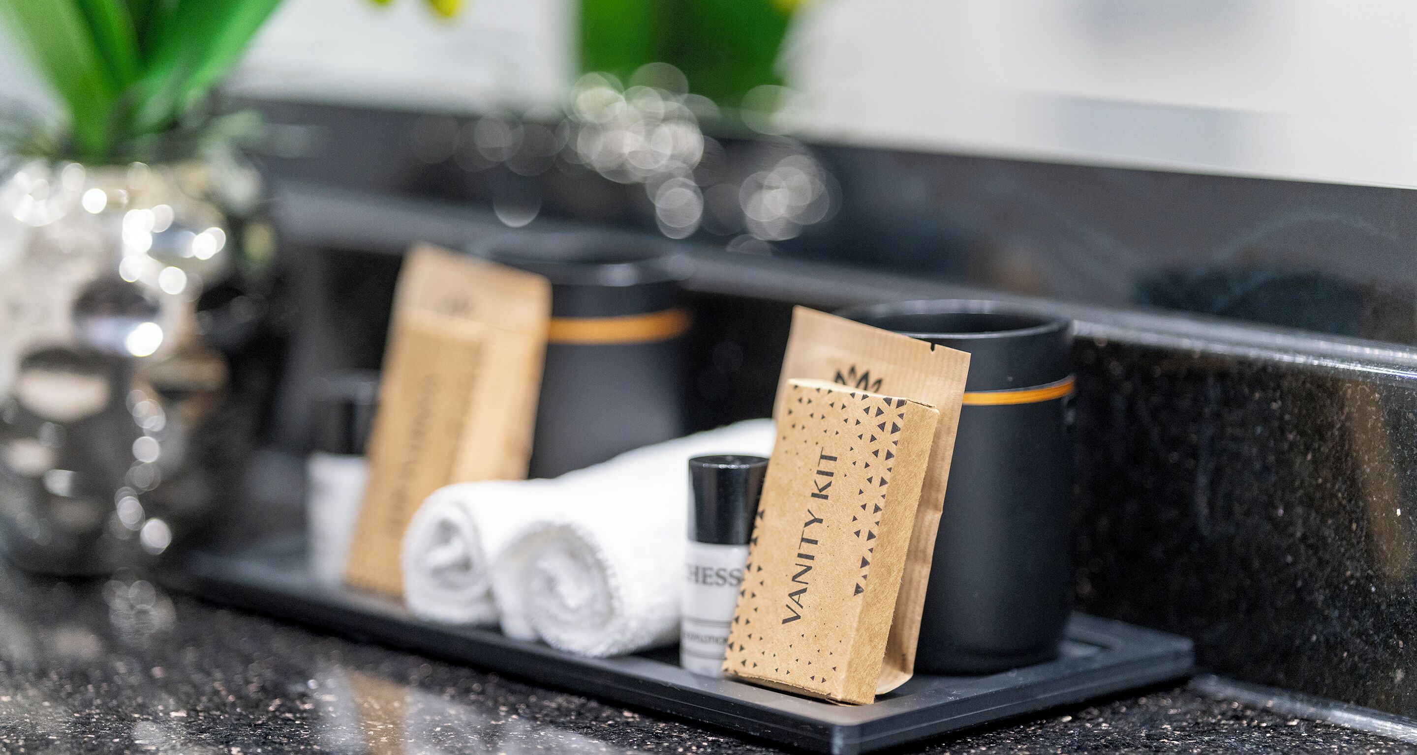 A tray with a towel, a black mug, and a brown paper bag labeled "Vanity Kit" on a black countertop.