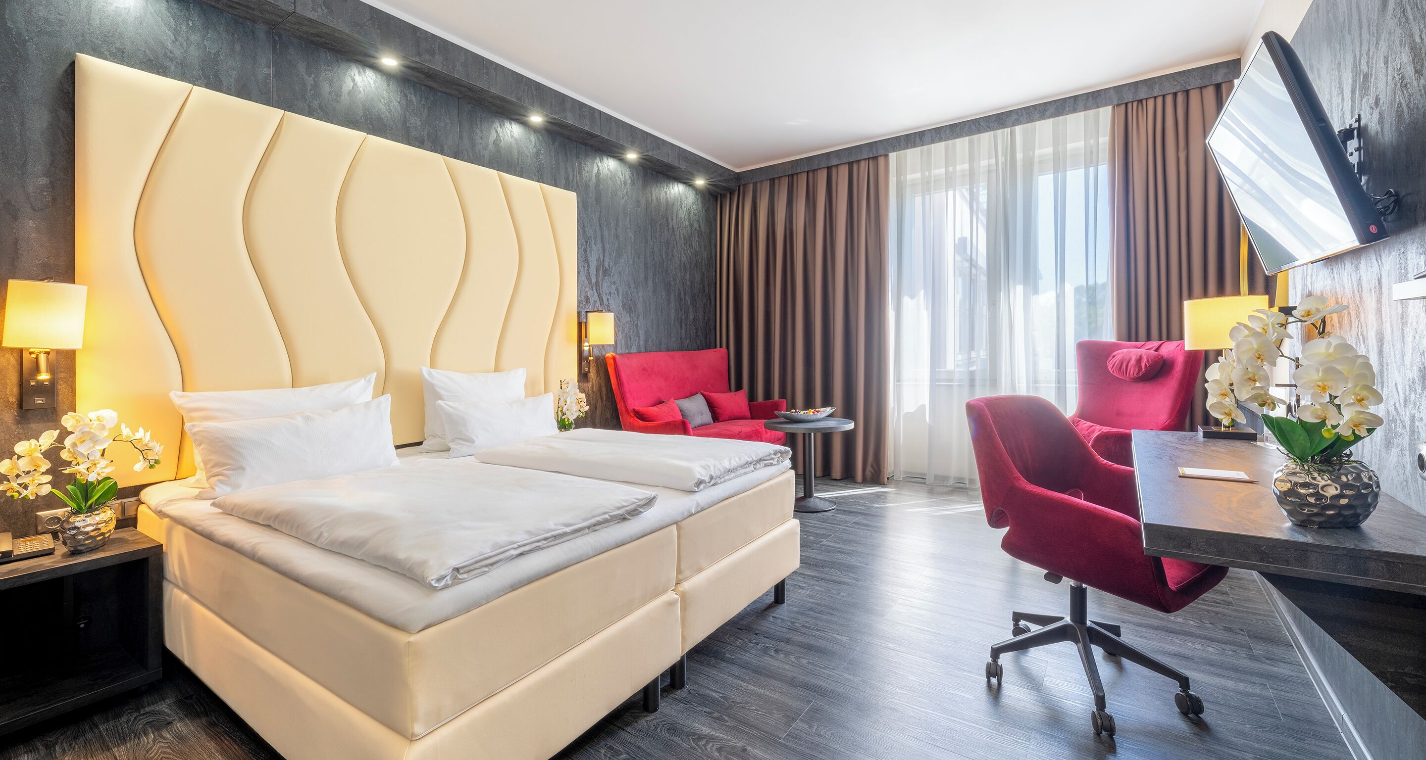 A modern hotel room with a large bed, a desk with a chair, and a TV mounted on the wall.