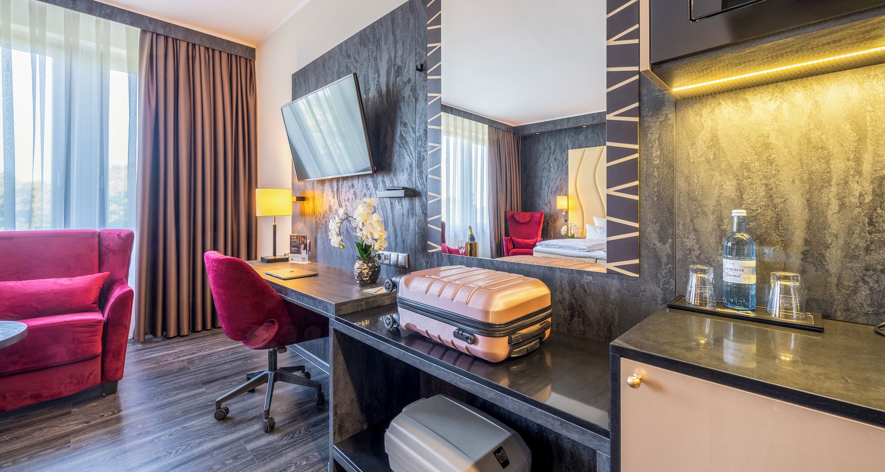 Habitació d'hotel amb escriptori, una cadira vermella, un llit, televisor fixat a la paret i un minibar.