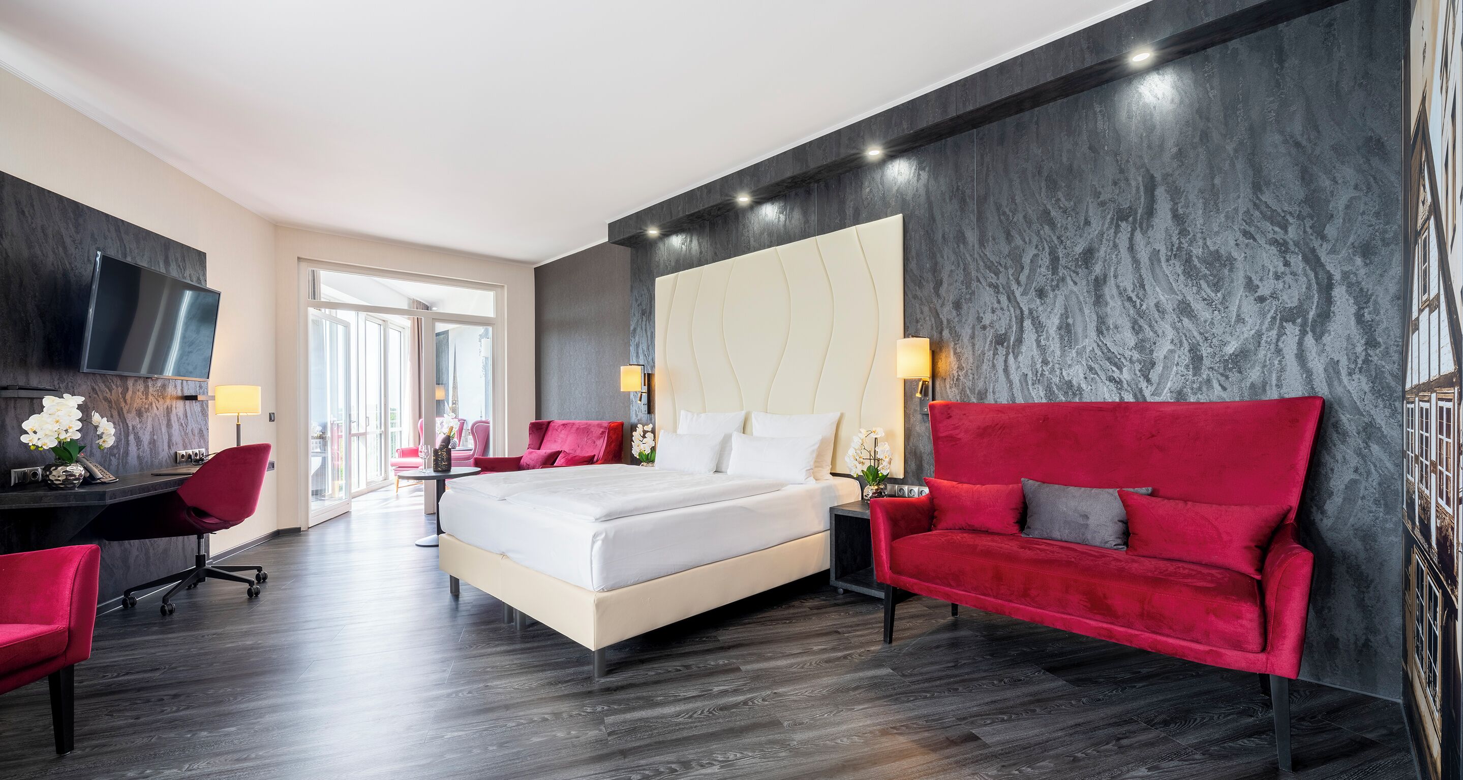 Una habitación de hotel moderna con una cama grande, un sofá rojo, un escritorio y un televisor.