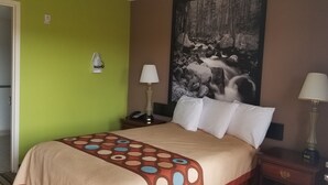 Quarto de hotel com cama, duas luminárias de cabeceira, mesa de cabeceira, telefone e uma pintura grande com tema de floresta na parede.
