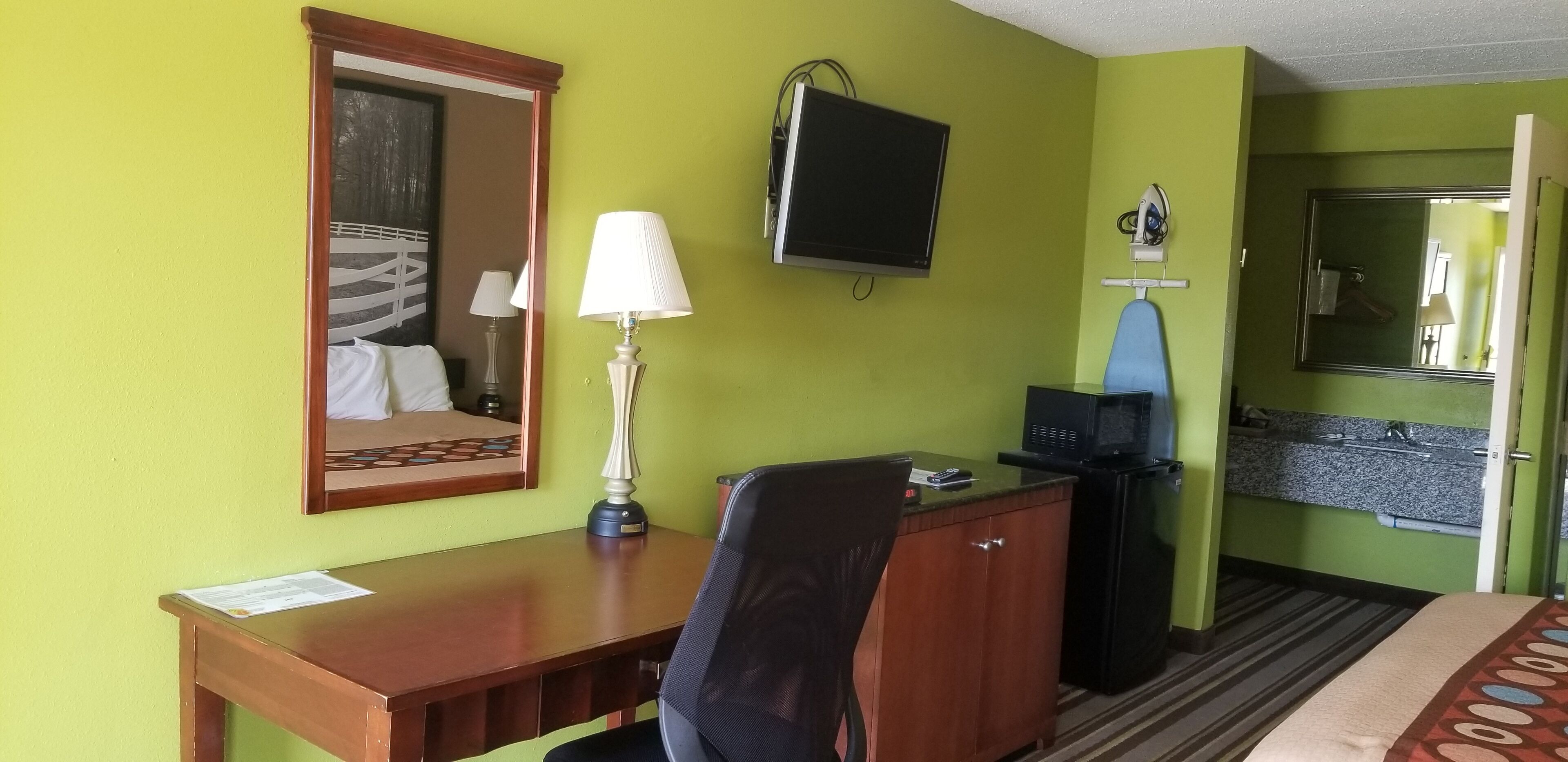 Une chambre d’hôtel équipée d’un bureau en bois, d’une chaise, d’une télévision, d’un miroir et d’un four à micro-ondes.