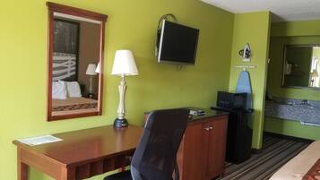 Quarto de hotel com escrivaninha de madeira, uma cadeira, televisão, espelho e micro-ondas.