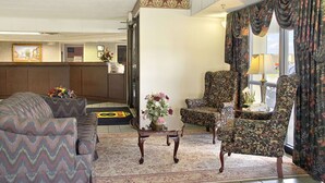 Um hall de entrada com uma mesa de recepção, uma poltrona estampada de flores, um sofá com padrão e uma pequena mesa com flores.