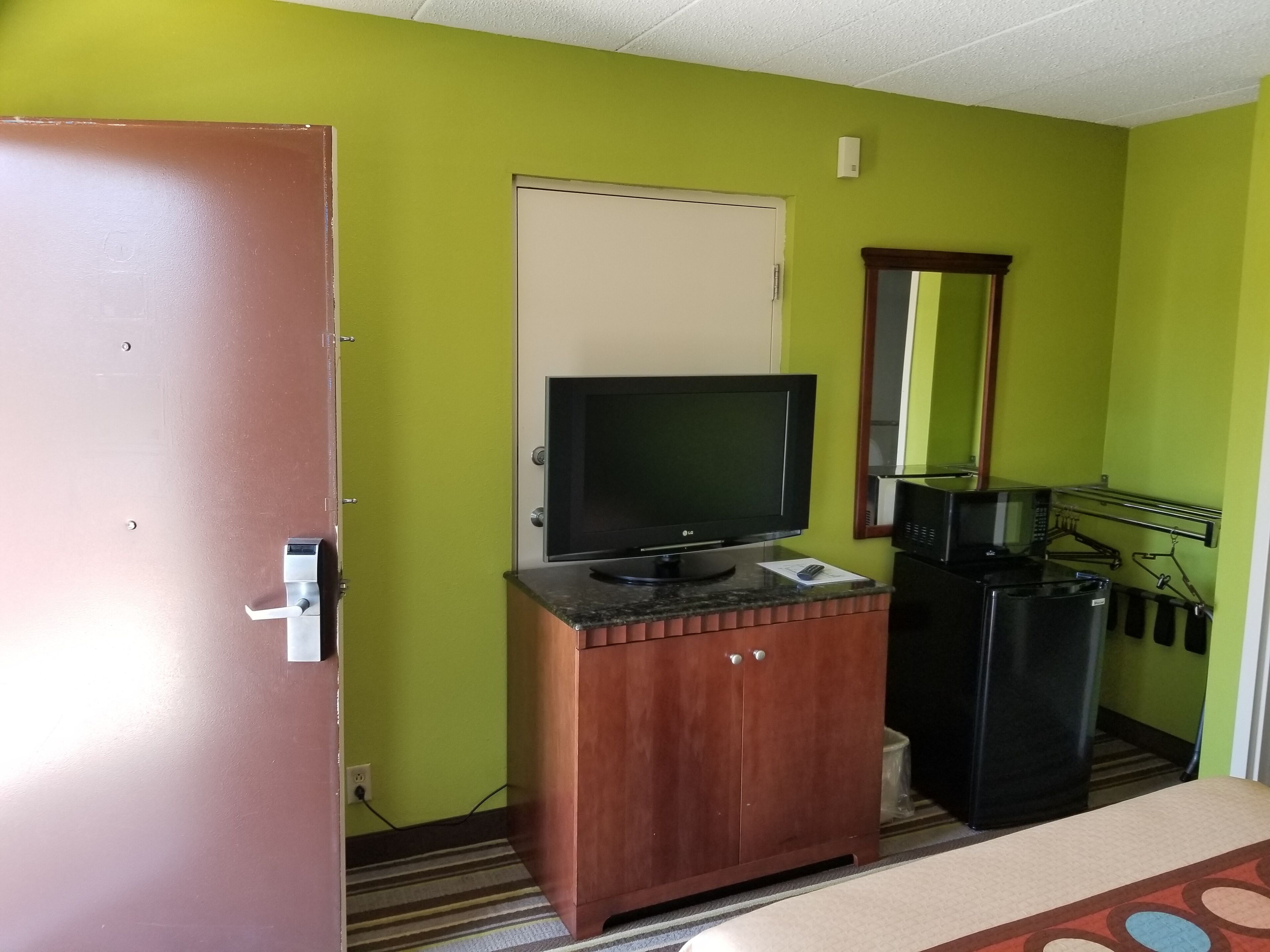 Una habitación con un armario de madera, televisor, microondas y refrigerador.