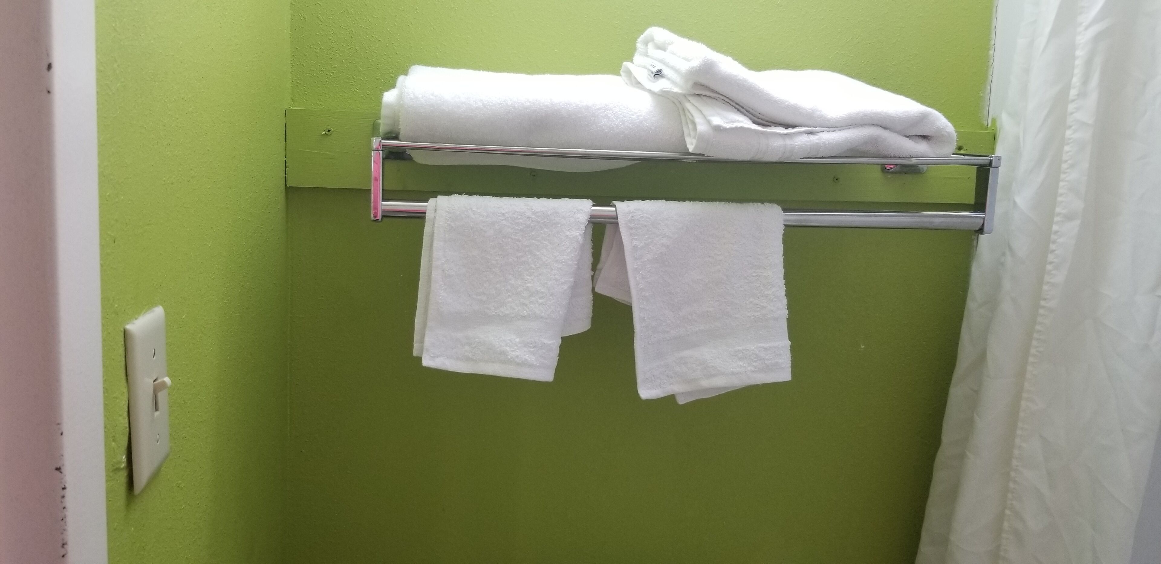 Un baño con paredes verdes, un perchero con toallas dobladas y una cortina de ducha blanca.