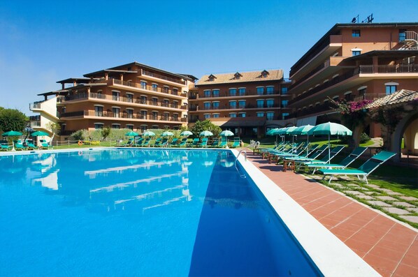 A hotel with a swimming pool, sun loungers, and umbrellas.