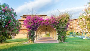 An arched pathway leading to a building with balconies, surrounded by lush greenery and flowering plants. - Resort Marina di Castello Golf & SPA (Castel Volturno)