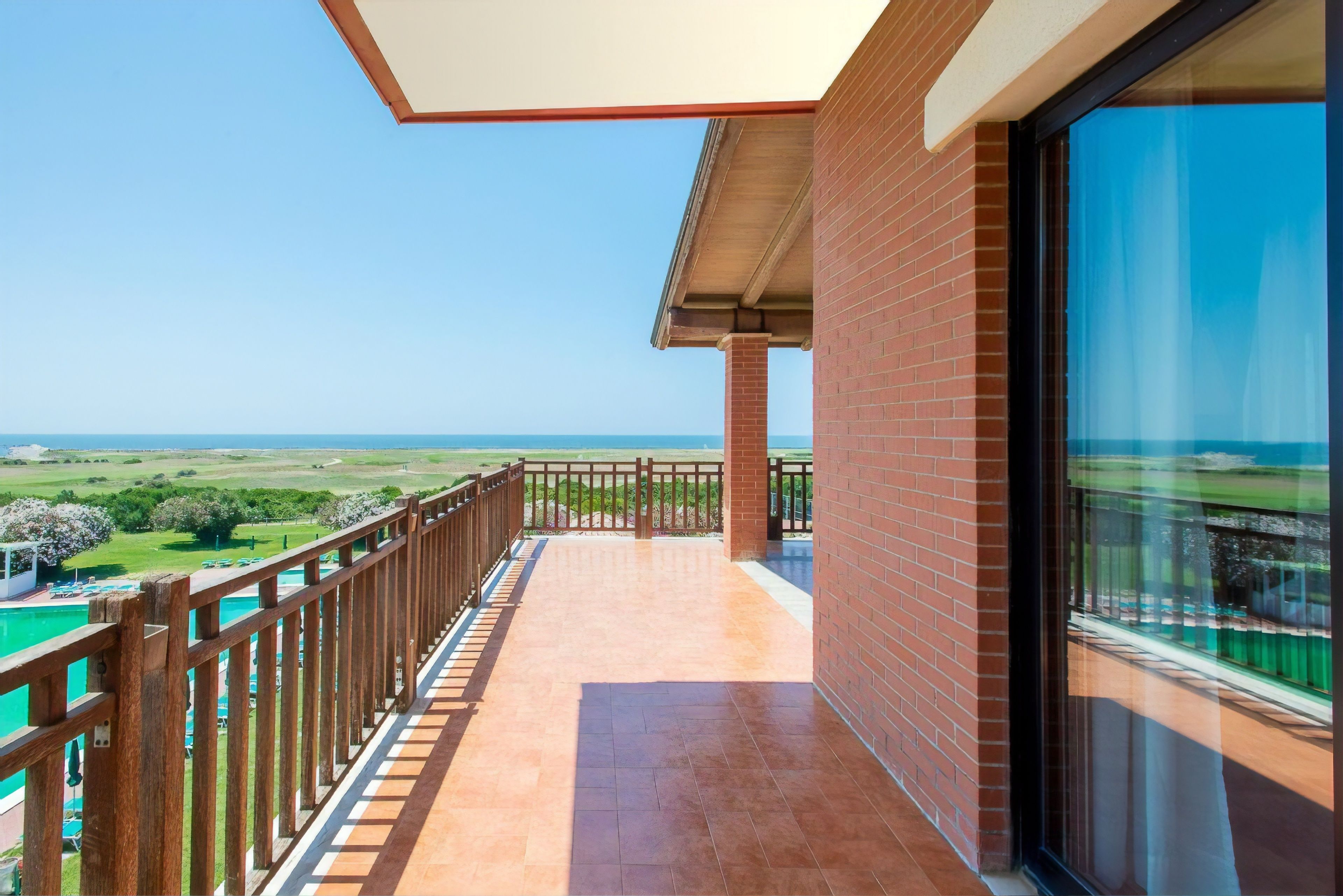 A balcony with a view of the sea, a brick wall, and a wooden railing.