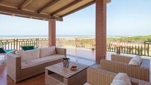 A covered outdoor seating area with wicker furniture, a cushioned sofa, and a table with a drink and fruit. - Resort Marina di Castello Golf & SPA (Castel Volturno)