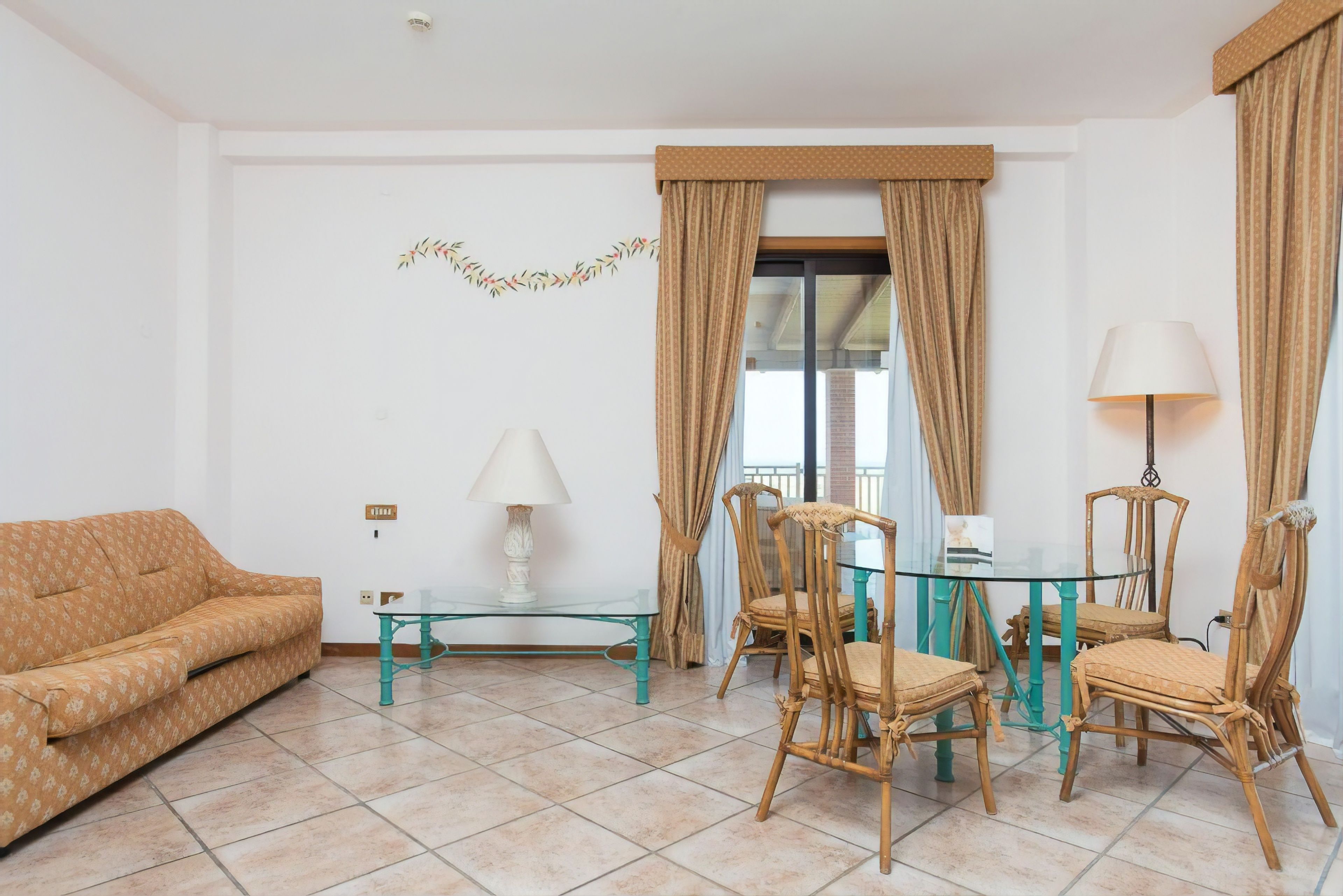 A living room with a sofa, a glass coffee table, a dining table with chairs, and a lamp.