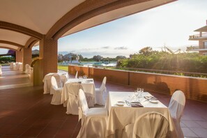 An outdoor dining area with tables set for a meal, overlooking a pool and greenery.
