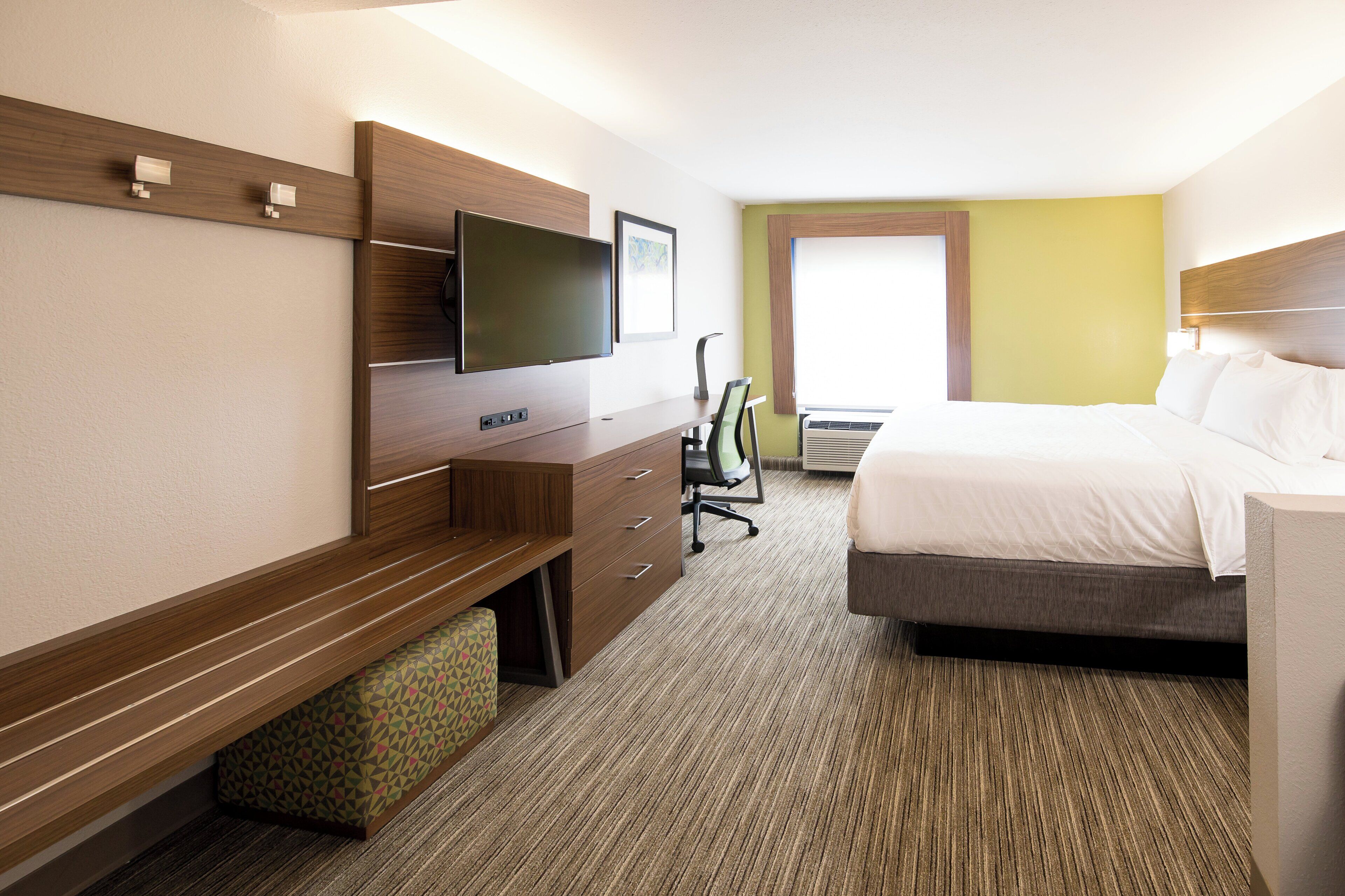 A hotel room with a bed, a desk with a chair, a television, and a window.
