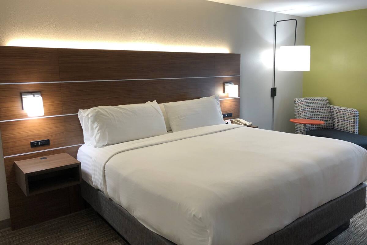 A hotel room with a large bed, bedside tables, a nightstand, a lamp, and a chair.