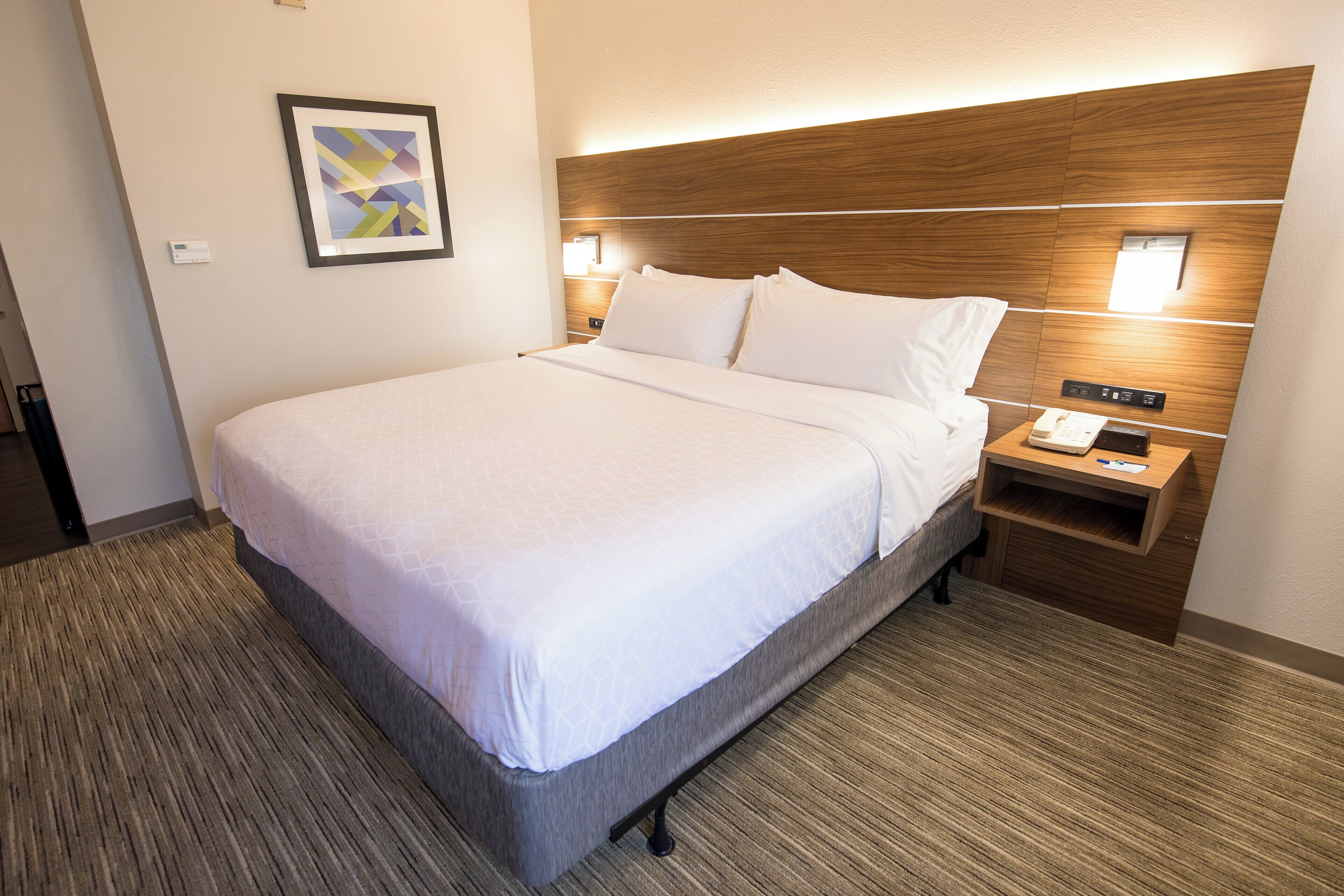 A hotel room with a large bed, a wooden headboard, a nightstand with a phone, and a wall-mounted light.