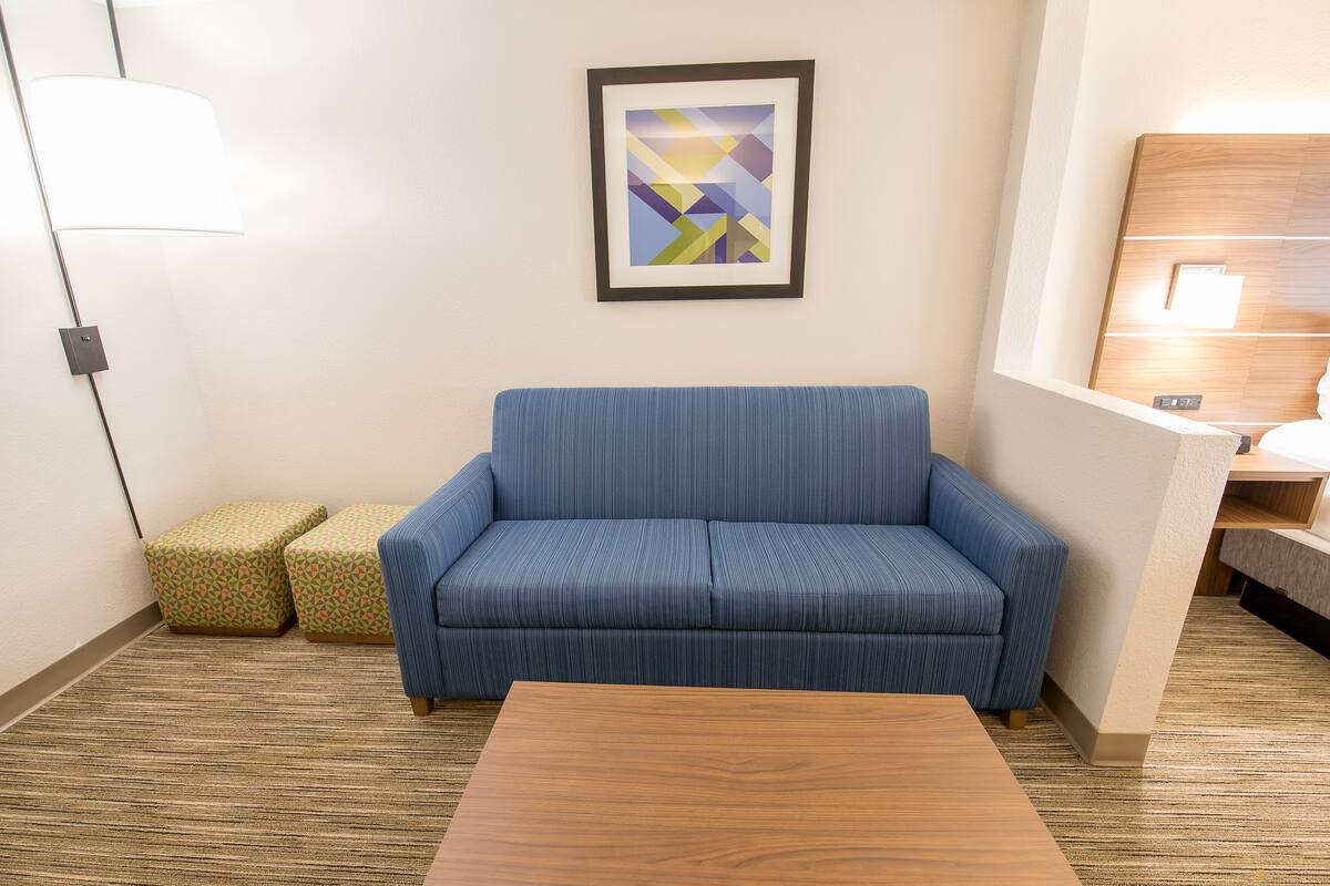 A modern hotel room with a blue sofa, a wooden coffee table, and a geometric art piece on the wall.