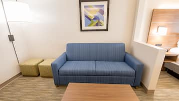 Quarto de hotel moderno com um sofá azul, uma mesa de centro de madeira e uma obra de arte geométrica na parede.