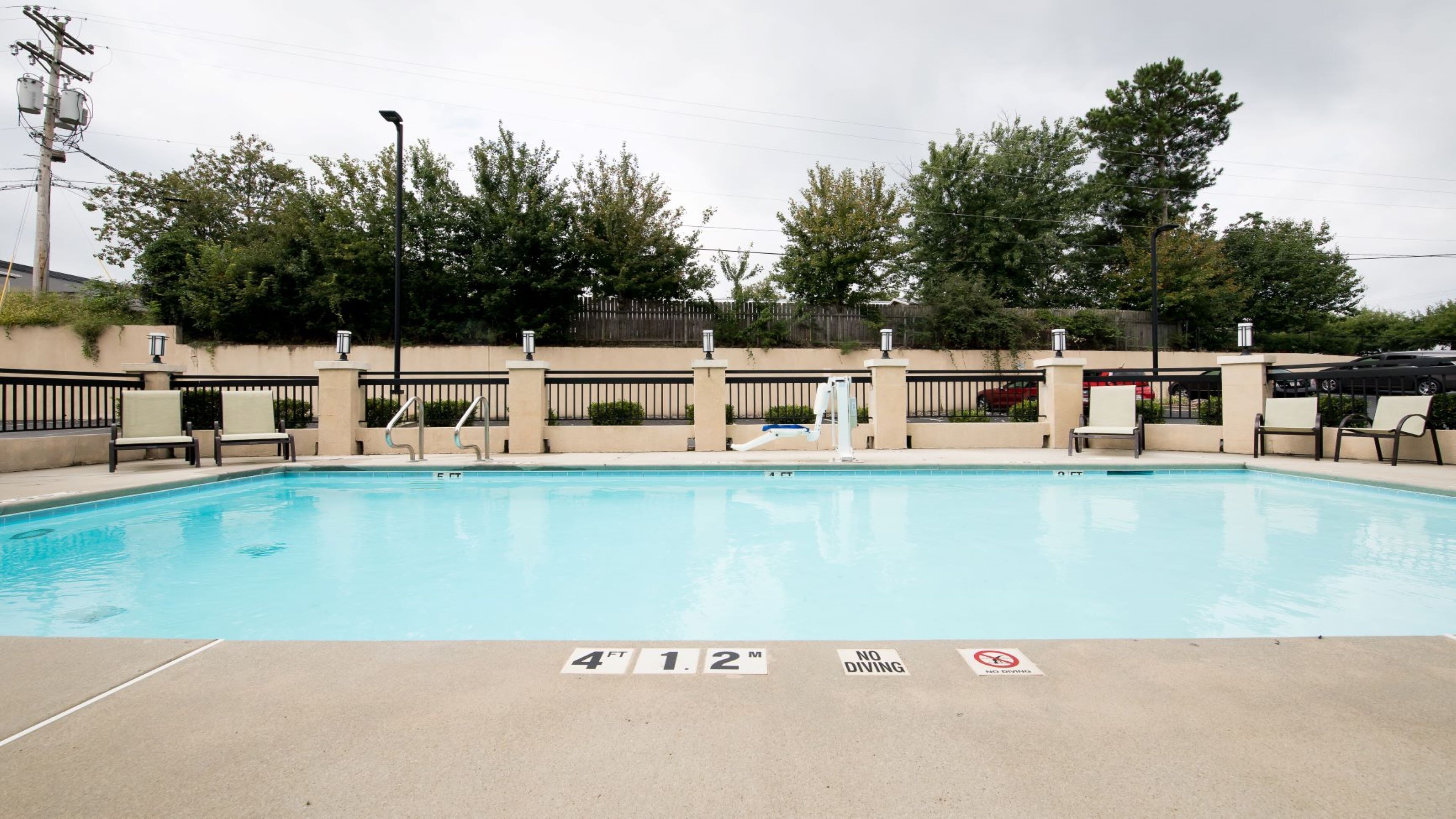 A rectangular swimming pool with a shallow end, surrounded by a low wall and a fence. There are lounge chairs and a lifeguard stand visible.
