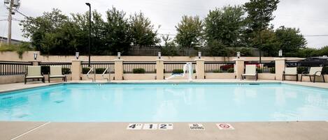 A rectangular swimming pool with a shallow end, surrounded by a low wall and a fence. There are lounge chairs and a lifeguard stand visible.