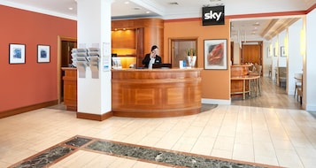 Zona de recepción de un hotel con un mostrador de madera, un cartel con la palabra 'sky', obras de arte enmarcadas en las paredes y un suelo de baldosas de mármol.