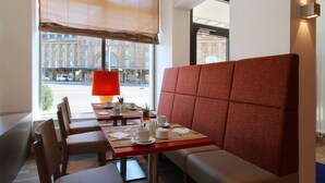 A modern dining area with a red cushioned booth, wooden chairs, and a table set with white cups and saucers. - Best Western Hotel Leipzig City Center (Leipzig)