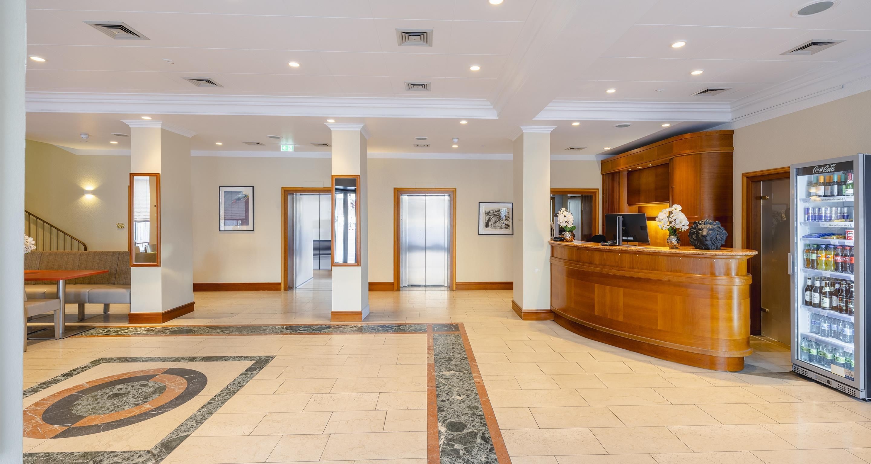 Eine Hotelhalle mit einer Rezeption, einem mit Getränken gefüllten Kühlschrank und einer Treppe zu einer weiteren Etage.
