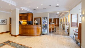 Un vestíbulo de hotel con una recepción, un refrigerador de Coca-Cola y un área de estar con mesas y sillas.