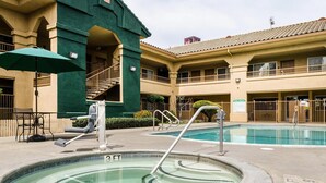 A pool area with a hot tub, a green umbrella, and a sign indicating pool rules. - Quality Inn & Suites Lathrop - South Stockton (Lathrop)