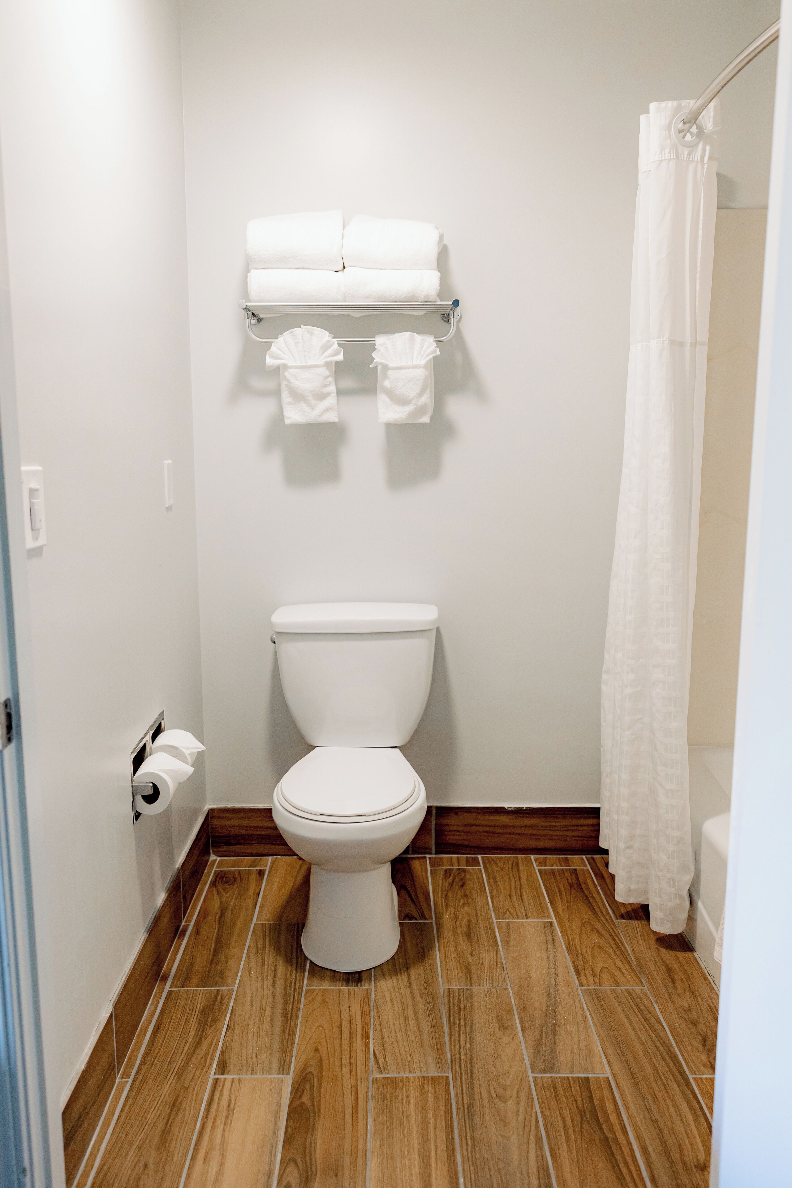 A bathroom with a white toilet, a towel rack with folded towels, and a shower curtain.