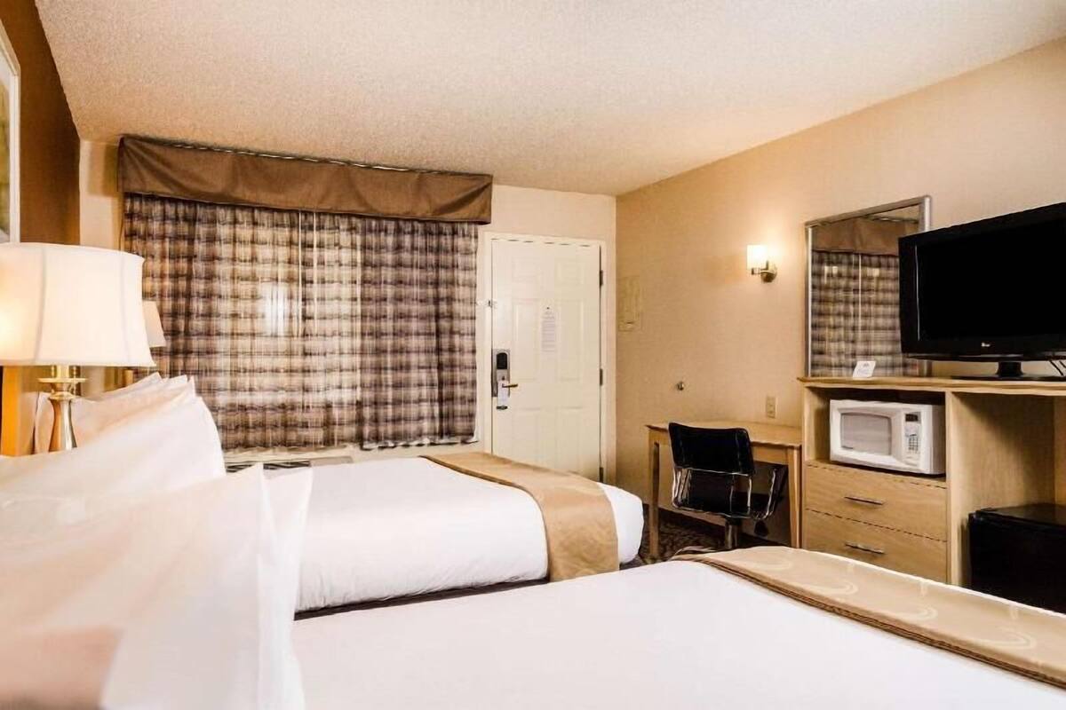 A hotel room with two beds, a television, a desk, and a microwave.