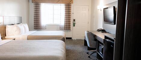 Quarto de hotel com duas camas, uma mesa, televisão e porta.
